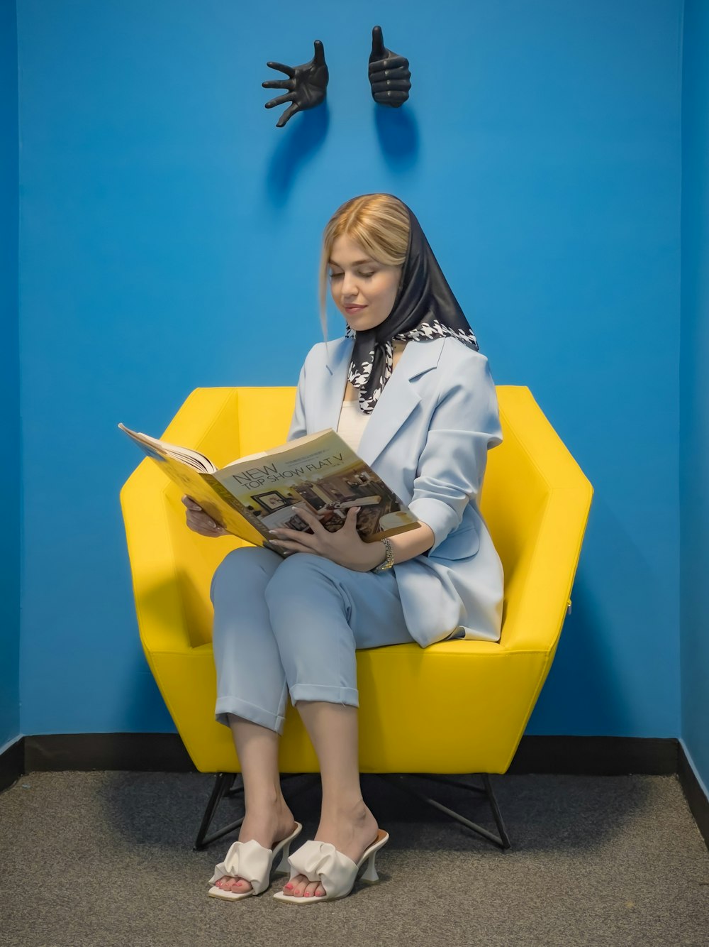 a woman sitting on a yellow chair reading a newspaper