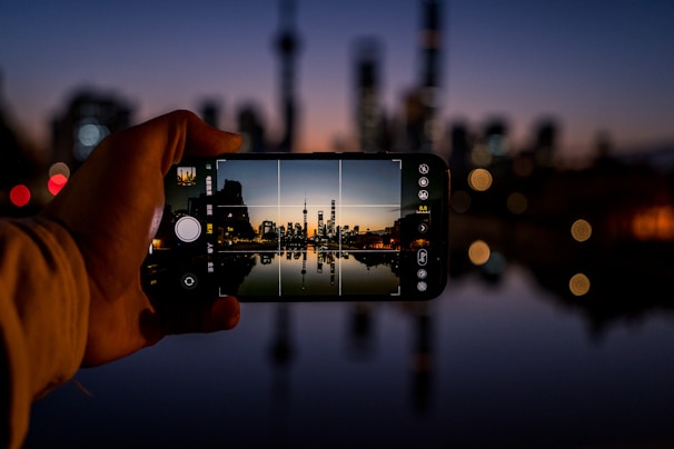 Person using a mini smartphone outdoors with a cityscape in the background.