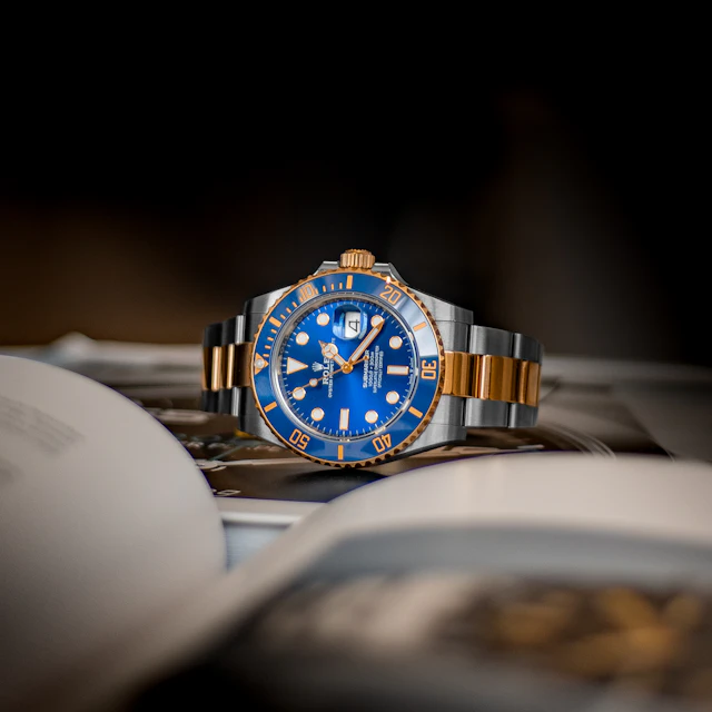 A blue and gold luxury wristwatch resting on an open book