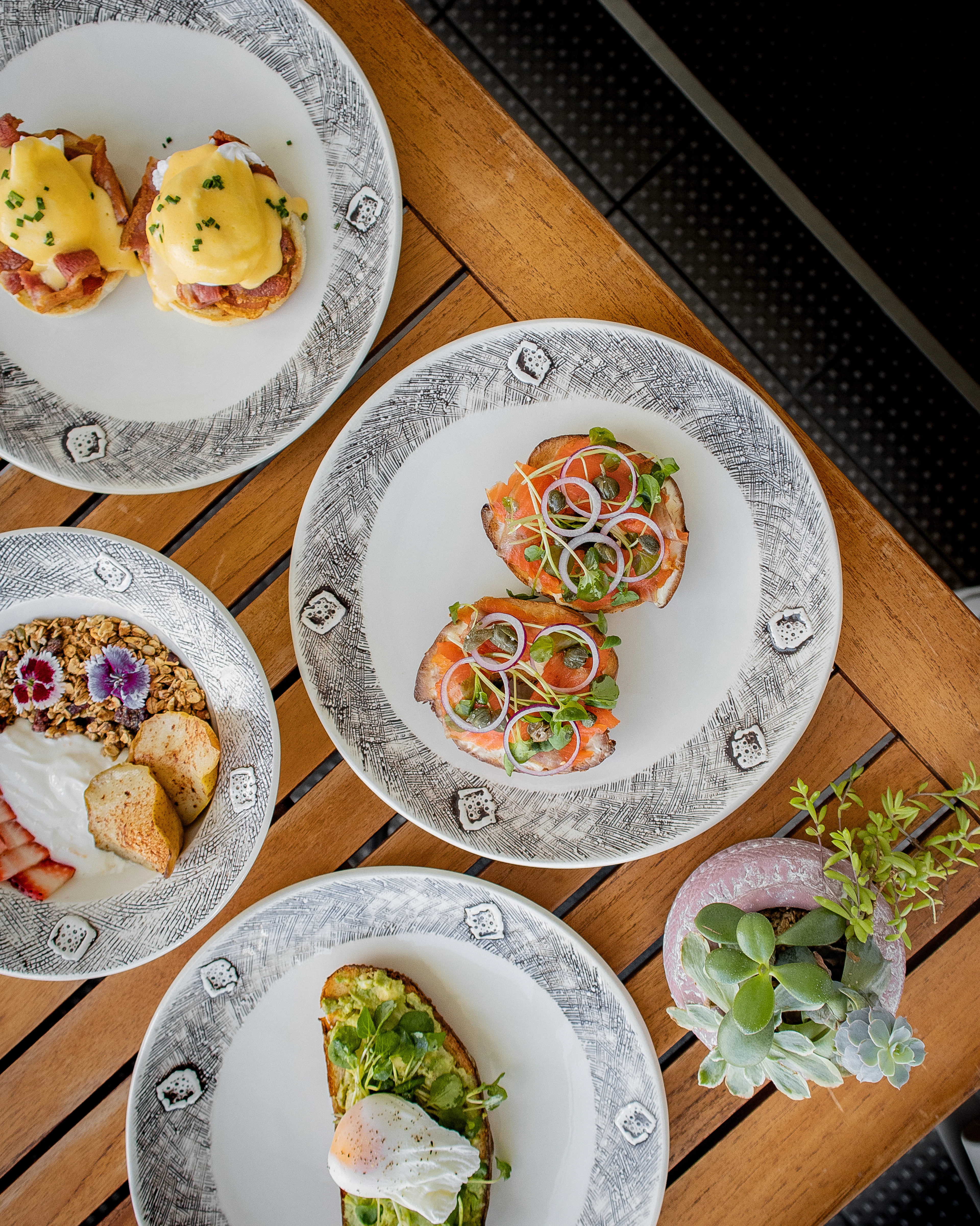 An overhead brunch spread at Off The Hook in Auckland CBD, New Zealand — eggs benedict, salmon and pickled-onion toasts, a granola bowl and avocado toast with a poached egg