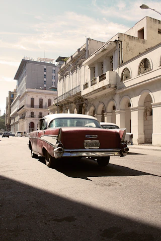 A vintage red Spanish car parked in front of a sunlit rustic building with Mediterranean details.