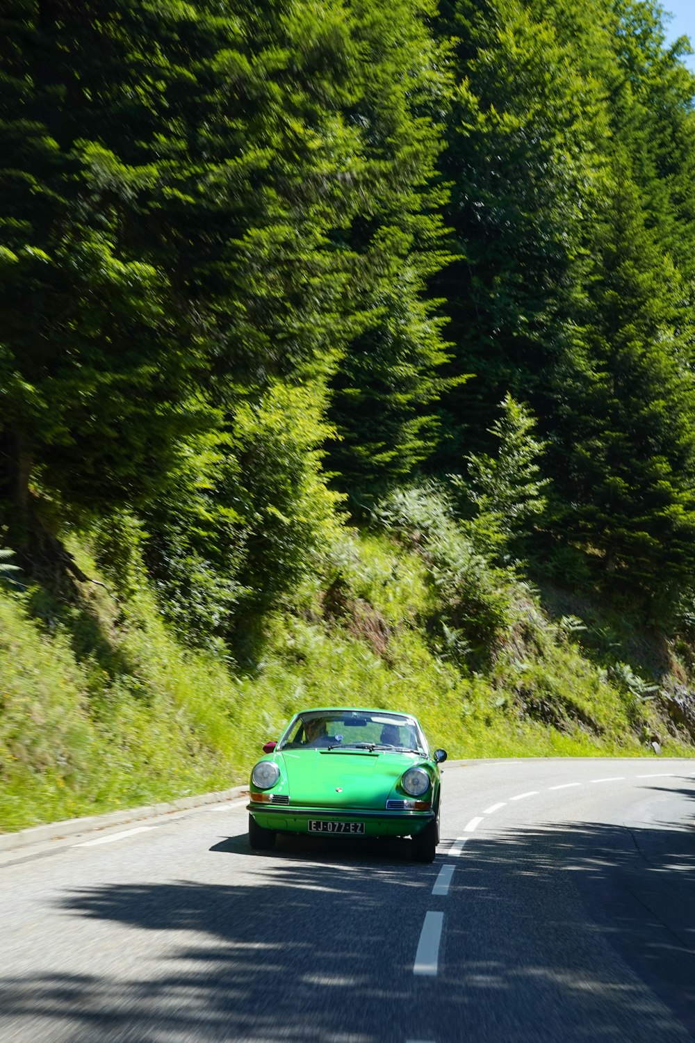 a green car on a road with trees on either side of it