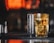 A can of Rush energy drink is placed on a bar mat, beside a glass filled with a golden-colored drink. The background is softly blurred, featuring warm, orange tones, suggesting a cozy bar or nightclub setting.