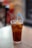 A glass filled with iced tea is placed on a wooden table. The drink is topped with a wedge of lemon and contains a silver spoon and a blue straw.