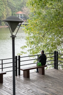 A solitary figure sitting on a bench overlooking a calm lake at sunset.