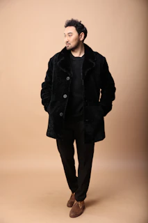 A sleek model wearing a charcoal oversized coat against a minimalist beige backdrop.