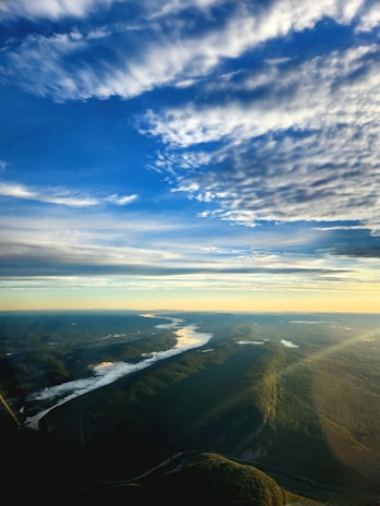 An overhead drone shot of a winding river cutting through lush green hills under a bright sky.
