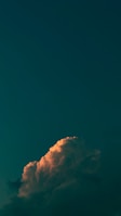 A large cloud formation is illuminated with soft, warm light against a backdrop of deep blue sky, creating a contrast between the glowing cloud and the dark surroundings.