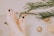 Feet with dark green nail polish are submerged in water, surrounded by festive elements like evergreen branches, a pine cone, small red and brown decorations, and a slice of lemon. A gold ornament floats nearby, creating a serene and holiday-themed atmosphere.