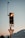 A traffic light with an illuminated amber light is mounted on a pole. Above it, a camera or sensor is attached to a tall antenna. Below the traffic light is a yield sign with a red border. A scenic backdrop of mountains is visible under a clear sky.
