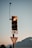 A traffic light with an illuminated amber light is mounted on a pole. Above it, a camera or sensor is attached to a tall antenna. Below the traffic light is a yield sign with a red border. A scenic backdrop of mountains is visible under a clear sky.