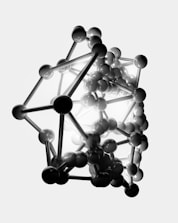A complex structure composed of numerous connected spheres and rods, forming a three-dimensional geometric shape. The arrangement resembles a molecular or atomic model, with a mix of dark and light elements creating a striking contrast.