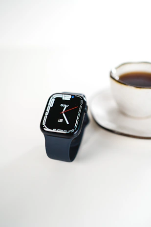 A sleek smartwatch resting on a minimalist wooden desk beside a laptop and a cup of coffee.