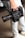A person is holding a professional RED digital cinema camera with a large lens and multiple attachments. The camera has visible branding, buttons, and handles, indicating it is designed for high-quality film production. The person is wearing light-colored jeans and sneakers.