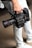 A person is holding a professional RED digital cinema camera with a large lens and multiple attachments. The camera has visible branding, buttons, and handles, indicating it is designed for high-quality film production. The person is wearing light-colored jeans and sneakers.