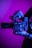 A person holds a professional digital camera with a large lens. The camera is branded as RED and features a sleek, modern design with various dials and grips. The lighting casts a magenta and blue hue over the scene, creating a dramatic effect.