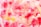 A vibrant abstract watercolor painting featuring a blend of pink, red, and yellow hues. The colors appear as swirling patterns and blotches, creating a dynamic and artistic effect. The texture is soft and fluid, with areas of light and shade adding depth.