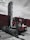 A large industrial vehicle designed for lifting and moving heavy objects is positioned next to several stacked shipping containers. A person wearing a protective suit and helmet is climbing onto the machine, which is painted primarily red and white. The overcast sky adds a muted backdrop to the scene.
