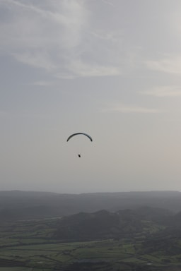A paramotor pilot soaring gently above the lush green hills of Shillong under a clear blue sky.