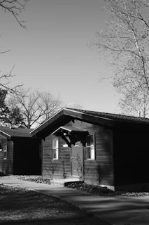Black and white drawing of a cozy countryside cottage surrounded by trees.