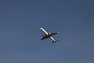 A commercial airplane flying against a clear, deep blue sky, captured from below. The airplane is predominantly white with visible engines and wings.