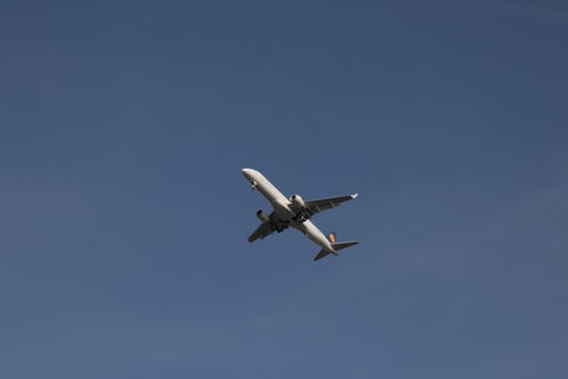 A commercial airplane flying against a clear, deep blue sky, captured from below. The airplane is predominantly white with visible engines and wings.