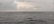 A vast expanse of ocean under a cloudy sky, with a distant view of an offshore oil rig and a ship on the horizon. The sea appears to be relatively calm despite the overcast weather.