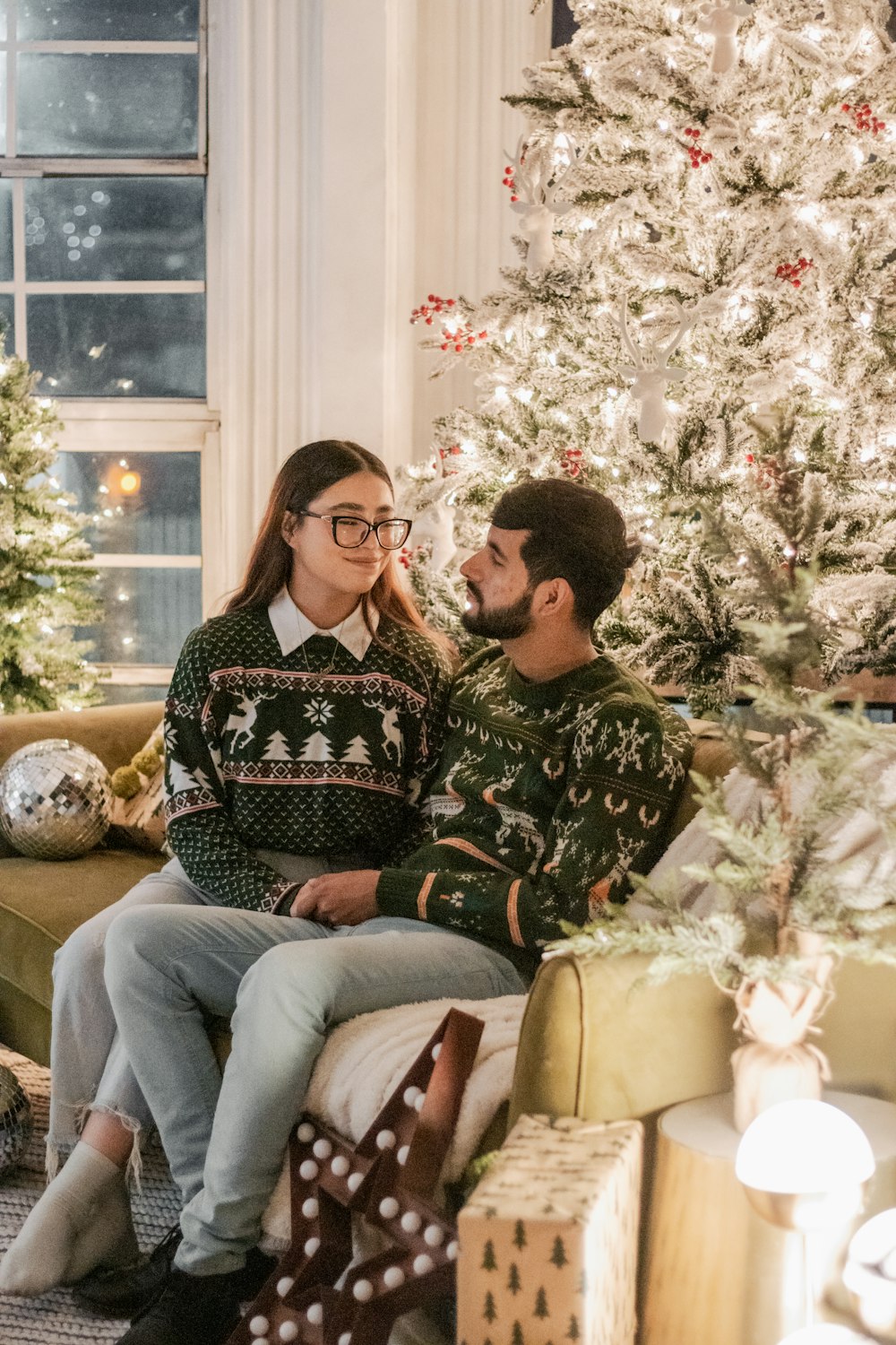 a man and woman sitting on a couch in front of a christmas tree