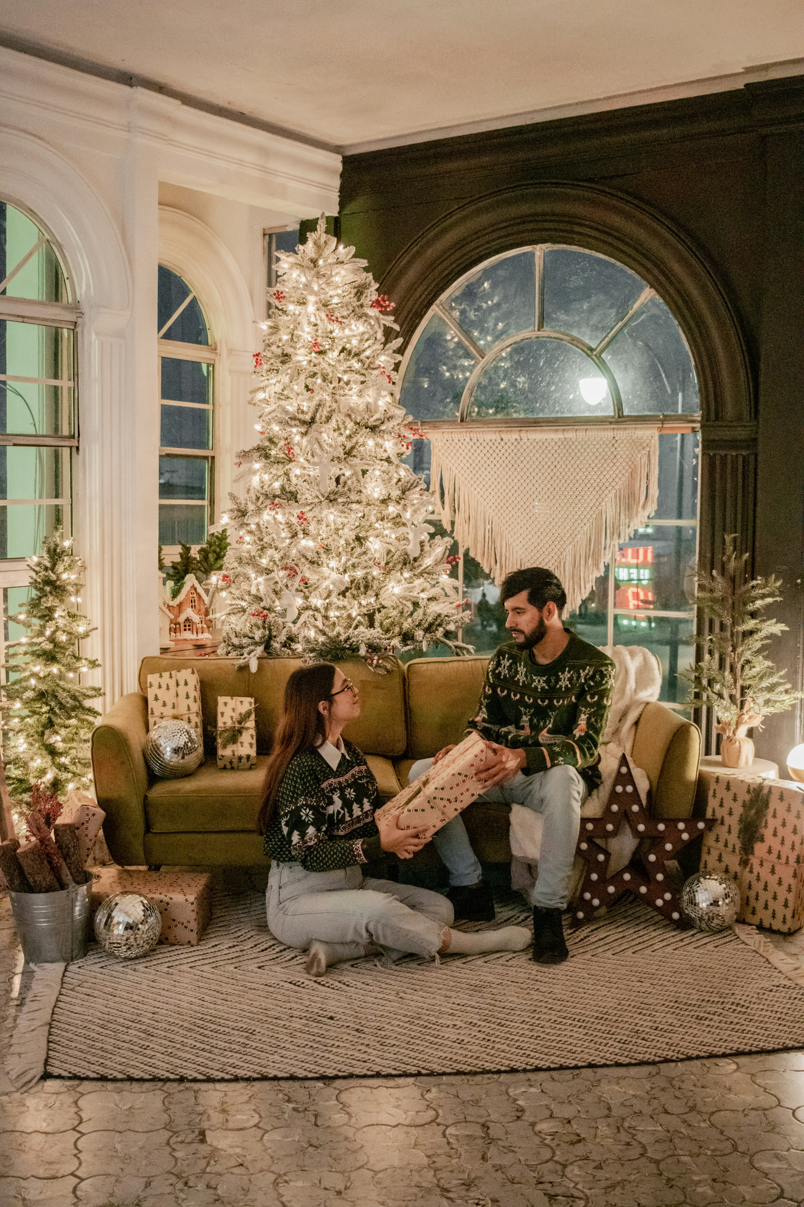 Cozy Christmas scene, warm fairy lights, two people sharing gifts near a decorated tree, soft candlelight glow