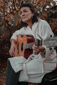 Hands gently strumming an acoustic guitar outdoors, surrounded by golden leaves swirling in a crisp breeze.