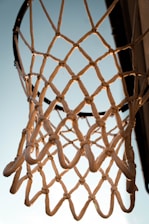 Close-up of a vibrant, durable basketball net hanging on an outdoor court under a bright sky.