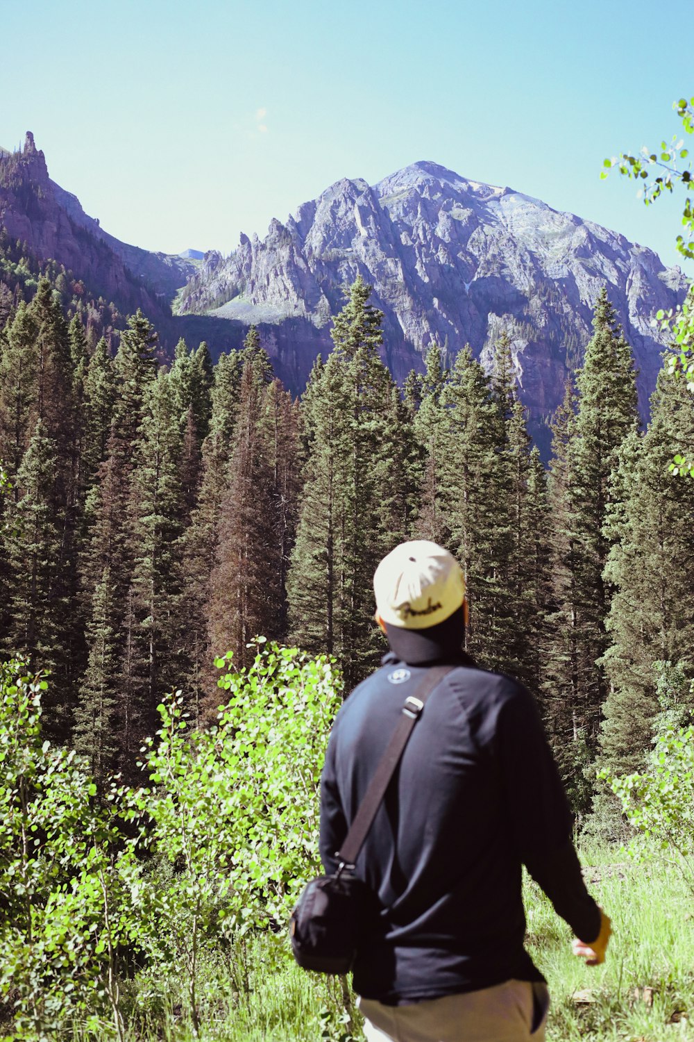 a man standing in a field with trees and mountains in the background