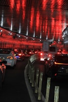 A tunnel filled with vehicles, predominantly cars and a truck, under a ceiling lined with reflective red lights. Lines of reflective barriers separate the lanes as traffic moves through the dimly lit passage.