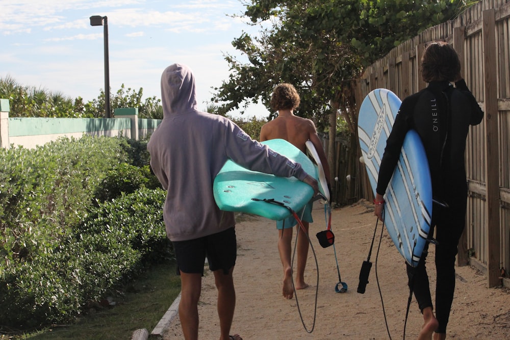 a group of surfers walk down a sidewalk