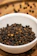 Close-up of fresh black peppercorns spilling from a rustic wooden bowl.