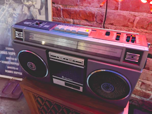 Close-up of a hand holding a headphone jack plugged into a vintage boombox with graffiti in the background.