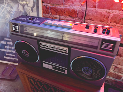 Close-up of a hand holding a headphone jack plugged into a vintage boombox with graffiti in the background.