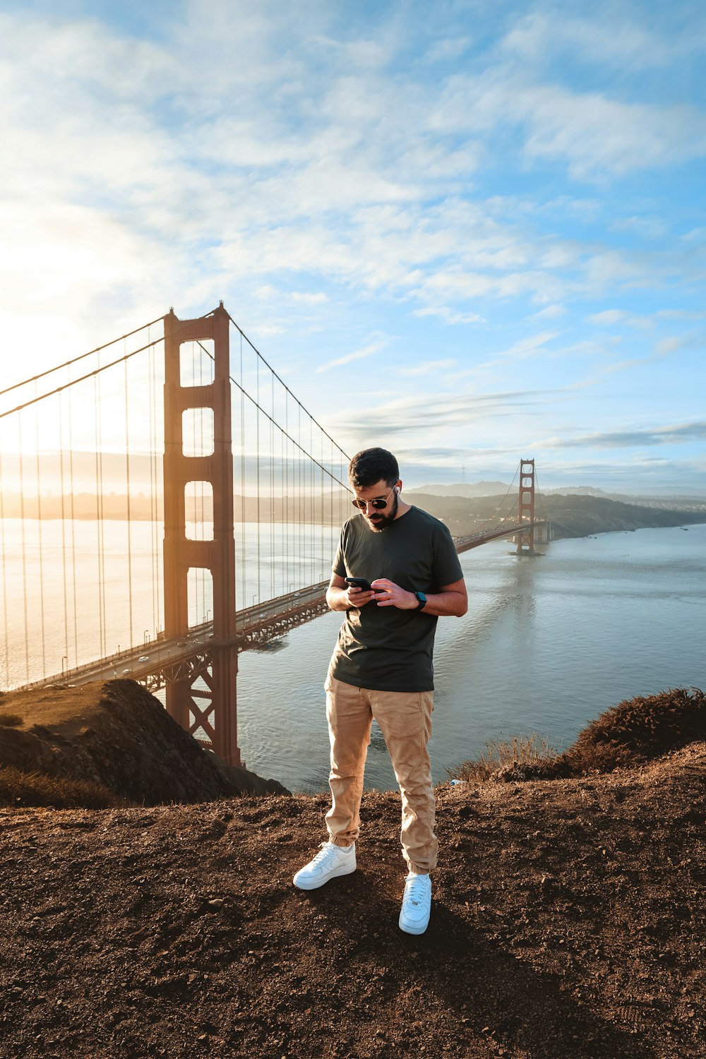 a man standing on a cliff with a large bridge in the background