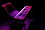 A vibrant, purple-lit scene featuring a synthesizer keyboard on a stand accompanied by a chair. The background is dark, highlighting the colorful lighting on the instruments.