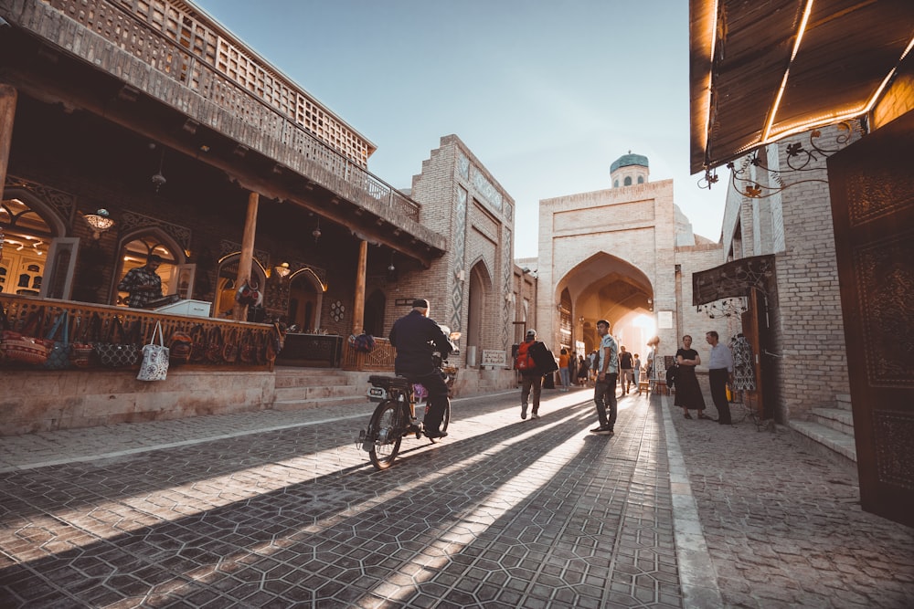 a person riding a bicycle on a brick road between buildings