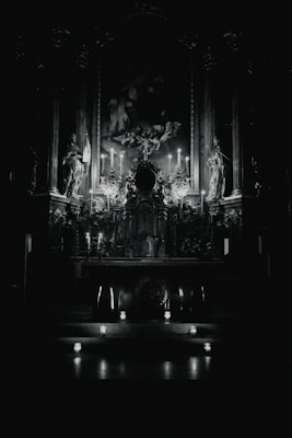 An ornate altar in a dimly lit religious setting, featuring statues and lit candles around a central painting. The atmosphere is enhanced by the subtle glow of the candles, creating a dramatic play of light and shadows.