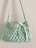 A small, handmade crochet bag with a textured pattern and a single strap. The bag features a decorative white ribbon tied into a bow on the front.