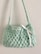 A small, handmade crochet bag with a textured pattern and a single strap. The bag features a decorative white ribbon tied into a bow on the front.