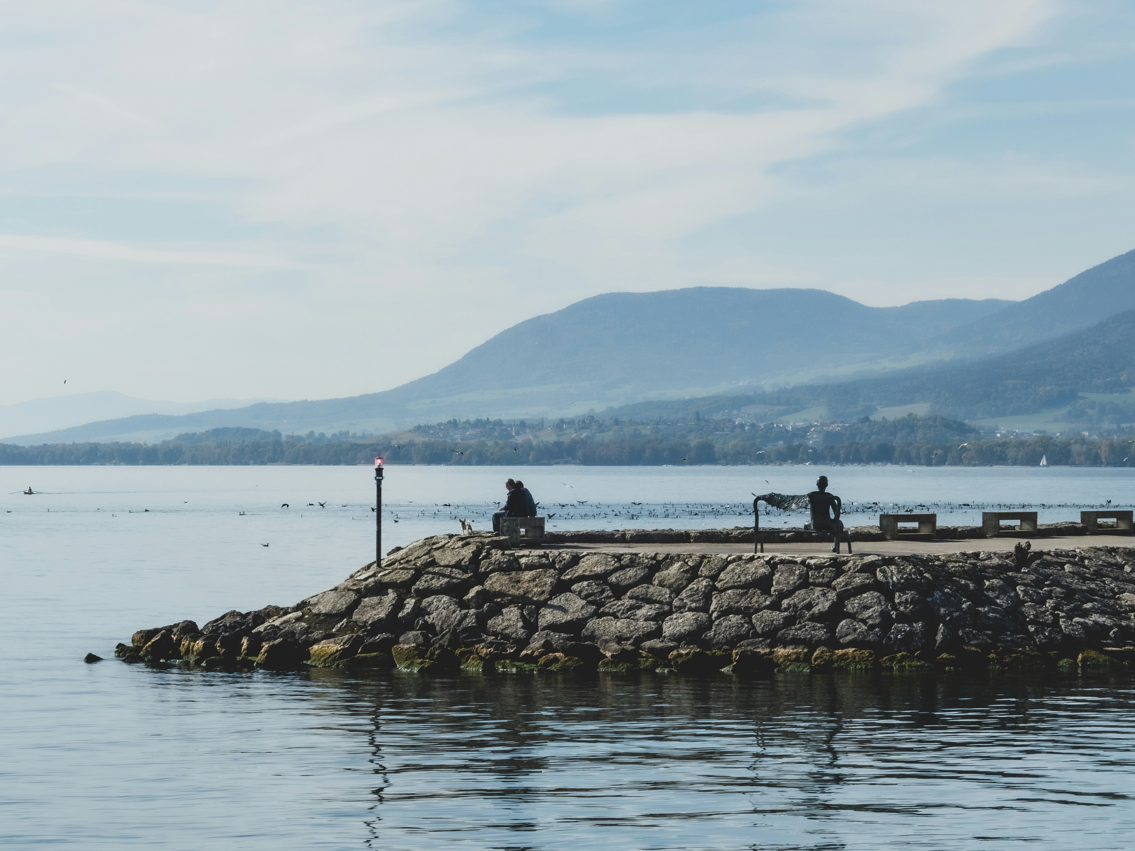 a couple people sitting on a rock wall by a body of water