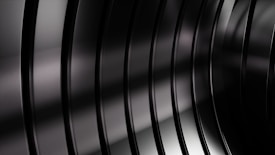 Smooth, reflective black metallic surfaces form parallel curved lines, creating a sense of depth and elegance. The lighting gently highlights the contours and textures.