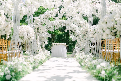 A beautifully decorated wedding aisle featuring a lush floral arch with white and pink flowers.