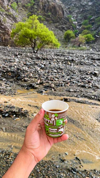 Hands of a lithologist examining rock samples beside a steaming cup of coffee.