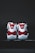 A pair of red and white athletic shoes with a glossy finish, placed on a dark surface. The shoes have white laces and a distinct logo on the heel.