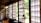 An interior with traditional Japanese sliding doors made of wood and frosted glass or paper, letting in ample natural light. Hanging close to the camera is a glass kerosene lamp, adding a rustic touch to the serene environment. The room has wooden floors and simple furniture, reflecting a minimalist aesthetic.