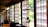 An interior with traditional Japanese sliding doors made of wood and frosted glass or paper, letting in ample natural light. Hanging close to the camera is a glass kerosene lamp, adding a rustic touch to the serene environment. The room has wooden floors and simple furniture, reflecting a minimalist aesthetic.